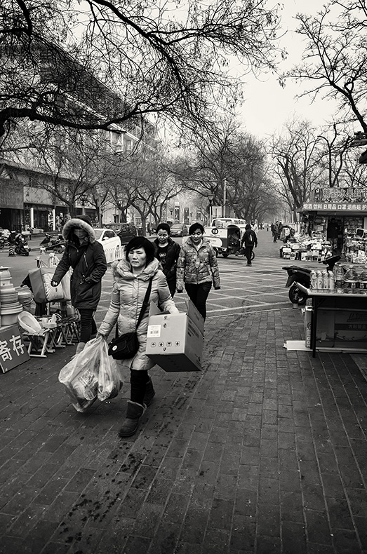 Chinese woman loaded with shopping walking along Yabao Road, Russia Town, Beijing, China.